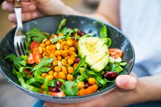 Woman holding salad bowl with greens, chickpeas and other fresh vegetables.