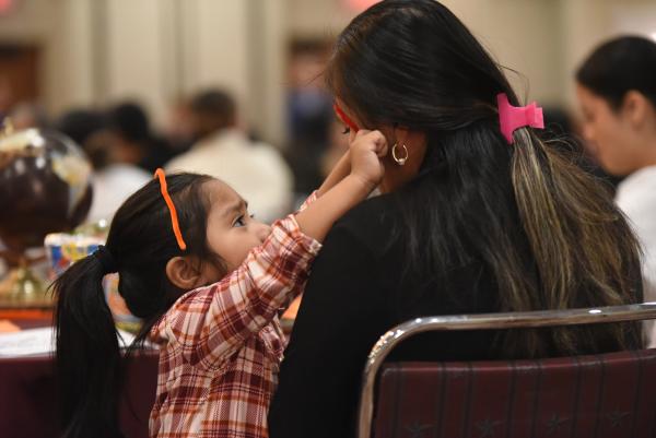 A young child playing with an adult female by wrapping a pipe cleaner across her forehead. The  young child also has a pipe cleaner wrapped over the top of her own head.