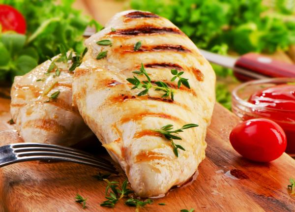 grilled chicken breasts stacked on a cutting board