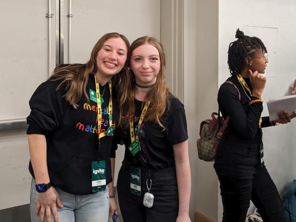 Two female youth standing next to each other, smiling. 